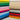 Stack of plain taupe 100% cotton fabric alongside various colorful cotton fabrics for crafts and sewing projects.